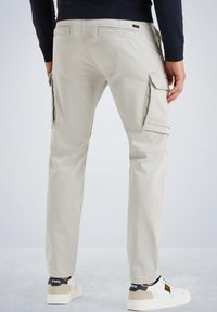 Beige cargo pants with side pockets, slim fit, and a smooth texture. Worn with white sneakers featuring black accents.