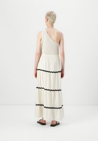 Asymmetrisk beige topp kombinert med en flytende hvit maxiskjørt med svarte bølgete striper. Båret med flate svarte sandaler.