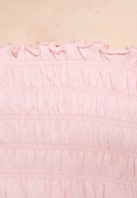 Κοντινό πλάνο σε ανοιχτό ροζ ρυτιδωτό ύφασμα με οριζόντια συγκεντρωμένα σχέδια και βολάν στην κορυφή.