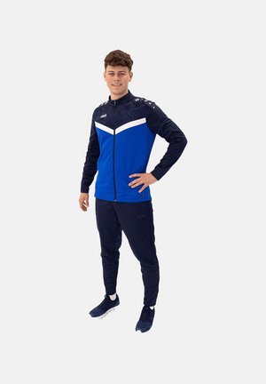 Athletischer Trainingsanzug mit einer blau-weißen Zip-Jacke mit schwarzen Akzenten, passenden blauen Hosen und navyblauen Sportschuhen.