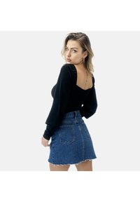 Body nero a maniche lunghe con dettaglio arricciato sulle spalle abbinato a una mini gonna di jeans a vita alta con orlo sfilacciato.