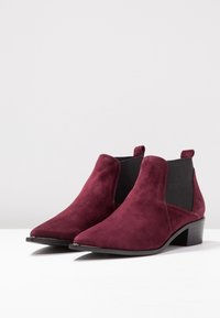 Burgundy suede ankle boots with a pointed toe, elastic side panels, and a low block heel, featuring a smooth texture and minimalistic design.