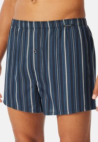 Marineblaue Boxershorts mit vertikalen Streifen in Blau- und Grautönen; elastischer Bund mit Knopfverschluss; weiche Stoffstruktur.