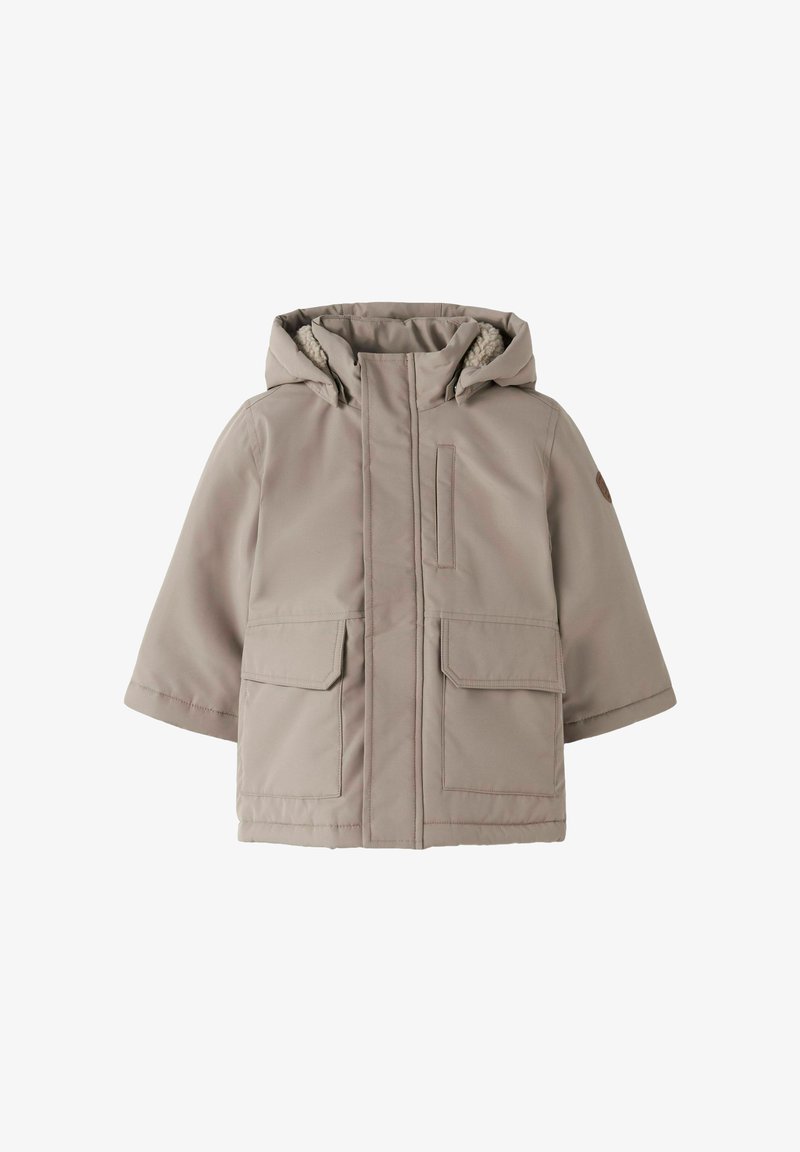 Beige kapučjaka ziemas jaka ar priekšējo rāvējslēdzēju, divām lielām priekšējām kabatām un mīkstu iekšējo oderi. Iezīmē moderna, kvadrāta formas dizainu.