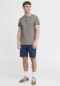 Grå T-skjorte med kort erm og rund hals, med en tre-knapps placket, kombinert med blå denimshorts og brune joggesko.