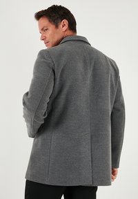 Sivi plašč iz volnene mešanice s krojem po meri, z izrezanim ovratnikom in subtilnimi podrobnostmi na ramenih, prikazan od zadaj na nevtralnem ozadju.