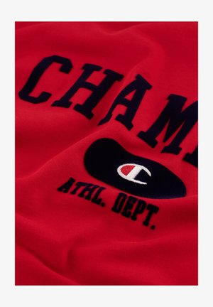 Rode katoenen sweatshirt met grote marineblauwe tekst "CHAMP" en "ATHL. DEPT." en een zwart ovaal logo met een wit en rood embleem.