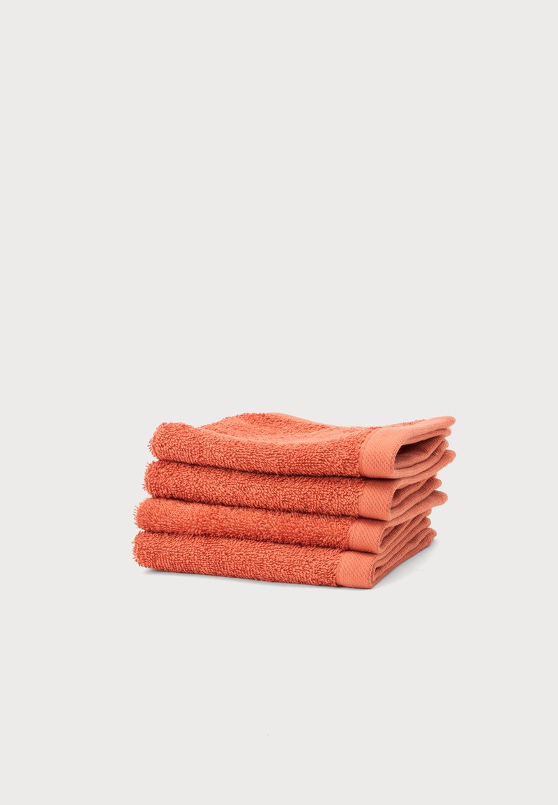 Quatre lavettes de couleur corail soigneusement pliées empilées sur un fond uni gris clair.