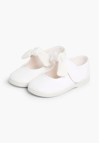 Weiße Leinenschuhe mit runder Zehenpartie, flacher Sohle und verstellbarem Klettverschluss, mit einer dekorativen Schleife am Riemen.