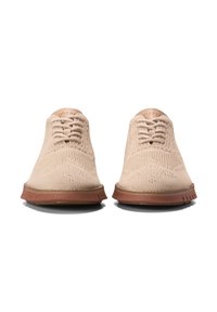 Scarpe beige lavorate a maglia con un design a profilo basso, caratterizzate da una tomaia texturizzata, sei occhielli per i lacci e una suola di gomma marrone.