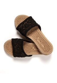 Chanclas negras con un diseño de encaje floral, suela marrón texturizada que presenta un patrón intrincado, estilo de punta abierta.