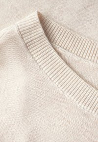 Maglione lavorato a maglia color beige chiaro con colletto a girocollo a coste e texture morbida. Presenta una finitura liscia e dettagli di cucitura minimi.
