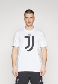 Hvid kortærmet t-shirt med et stort sort Juventus-logo i midten, lavet af blødt stof med rund halsudskæring.