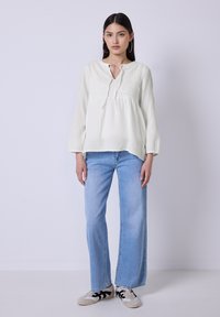 Hvid let bluse med struktureret mønster og snøredetalje ved halsudskæringen, parret med lyseblå vide jeans og grå sneakers med sorte accenter.