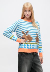 Sweter dzianinowy z niebiesko-białymi paskami, pomarańczowymi akcentami i wzorami brązowych królików, z prążkowanym dołem i geometrycznymi wzorami.