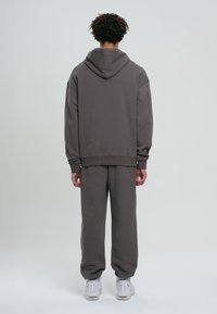 Sudadera gris y pantalones de chándal a juego, hechos de una tela suave. La sudadera tiene cordones y puños acanalados. Las zapatillas son blancas.