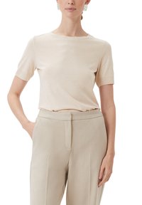 Beżowa bluzka z krótkim rękawem wykonana z miękkiego materiału, z okrągłym dekoltem. Połączona ze świadomością beżowymi spodniami o wysokim stanie z płaskim przodem.
