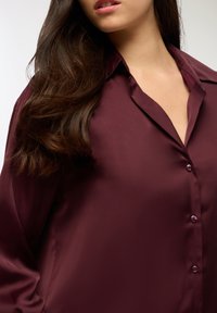 Burgundowa satynowa koszula z klasycznym kołnierzykiem, z przodem na guziki i długimi rękawami, o gładkiej, błyszczącej fakturze.