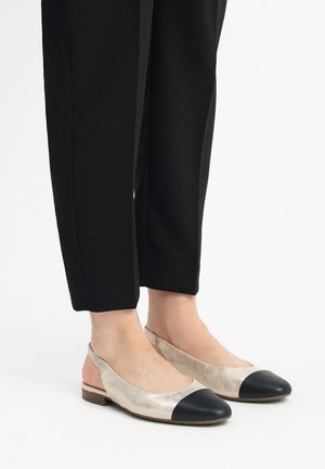 Zapatos planos con parte superior de oro metálico y puntera negra, con diseño de talón abierto y un tacón bajo; acabado texturizado, estilo minimalista.