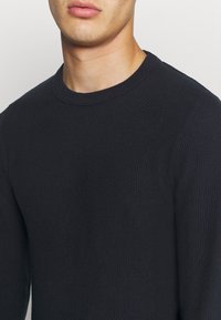 Marinblå stickad tröja med struktur, rund halsringning och lång ärm, med en ribbad krage och en figurnära design.