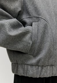 Grijze gevoerde jas met een ribbelrand, verborgen zijzakken en een soepele textuur, die een ontspannen pasvorm en gestructureerd ontwerp benadrukt.