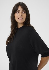 Czarny, oversize sweter z okrągłym dekoltem, teksturowana tkanina, krótkie rękawy, z zawiniętymi mankietami i luźnym krojem.