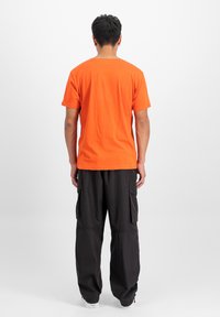 Camiseta de algodón naranja con mangas cortas, escote redondo, combinada con pantalones cargo negros que tienen grandes bolsillos laterales y un ajuste relajado.