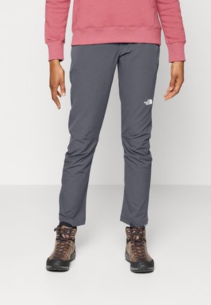 Gray outdoor pants made of lightweight material, featuring a slim fit and reinforced cuffs, paired with brown hiking boots and a pink sweatshirt.