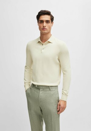 Light beige long-sleeve polo shirt with a collar, two buttons, paired with green textured trousers, featuring a tailored fit.