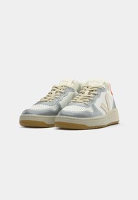 Low-top sneakers with white, gray, and beige panels, beige laces, gum soles, and a red accent on the heel side.