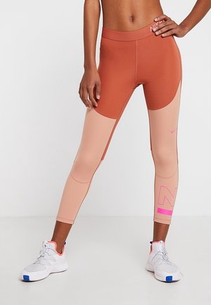 Leggings taille haute dans des tons rouille et nude avec une texture lisse, arborant un logo Nike rose et des détails de panneaux.