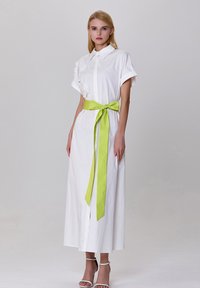 Robe midi blanche avec un col, des manches courtes, des embellissements floraux et une ceinture de taille verte vif. Tissu lisse et coupe droite.