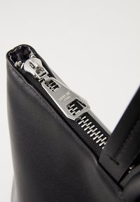 Zwarte lederen tas met een zilveren ritssluiting. Heeft een gestructureerd oppervlak en een slank ontwerp, waarbij de metalen hardware en stiksels worden benadrukt.