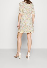 Blumenkleid im Mini-Stil mit Pastellfarben, kurzen Puffärmeln und einem Volant-Saum. Getragen mit klobigen Sandalen mit Absatz. Der Stoff scheint leicht zu sein.