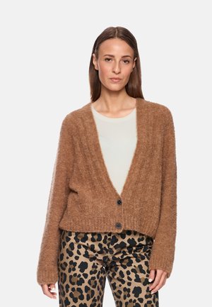 Brauner, flauschiger Cardigan mit tiefem V-Ausschnitt, zwei schwarzen Knöpfen und gerippten Bündchen, kombiniert mit beigefarbenen Hosen im Leopardenmuster.