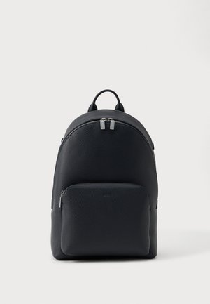 Fekete texturált bőr hátizsák két cipzáros rekesszel és egy felső fogantyúval, sima fehér háttér előtt.