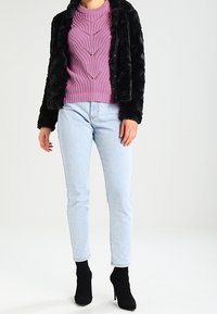 Zwarte nepbontjas, paarse gebreide trui met een textuurpatroon, lichtblauwe jeans en zwarte enkellaarsjes.