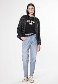 Chaqueta de plumas negra, mangas cortas, camiseta con logo, jeans de cintura alta de color azul claro y sandalias beige con suelas gruesas.