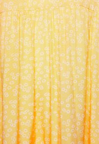 Abito in tessuto giallo con motivo floreale bianco, caratterizzato da pieghe e una texture leggera. Il design è semplice e morbido nell'aspetto.