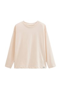 T-shirt beige à manches longues avec un petit tag en bas à droite portant la mention "APPORTER LA NATURE DANS VOTRE VIE."