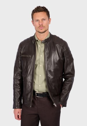 Brown leather jacket with a stand collar, zippered front, and stitching details on shoulders. Worn over a light green shirt.