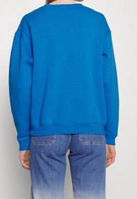 Blå sweatshirt med ribbade manschetter och nederkant, med en avslappnad passform och mjuk textur. Matchad med blekta blå jeans som visar subtila sömnadsdetaljer.