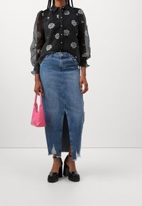Blusa nera trasparente con ricami floreali, abbinata a una gonna di jeans con uno spacco frontale. Accessoriata con una piccola borsa rosa e tacchi neri.