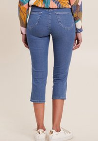 Jean capri bleu clair au design ajusté, longueur cropped et décoloration subtile. Comprend deux poches arrière et des ourlets cousus.