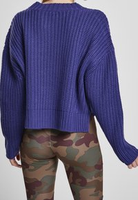 Fioletowy krótki sweter dziany o fakturowanym wzorze, z opuszczonymi ramionami i szerokim ściągaczem, zestawiony z legginsami w kamuflażu.