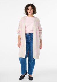 Gai bēšas garš kardigāns ar rozā rakstiem, apvienots ar gaiši rozā topu un augstu jostasvietu ziliem džinsiem. Strukturēta auduma, atvērta priekšpuses dizains.