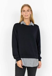 Schwarzer Kapuzenpullover, der über ein schwarz-weiß gestreiftes Hemd mit Kragen geschichtet ist. Hat lange Ärmel und eine lockere Passform. Sanfte Textur, lässiges Design.