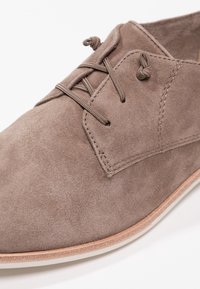 Chaussure à lacets en daim taupe avec peu de coutures et une semelle beige claire, montrée en gros plan vue en angle de dessus.