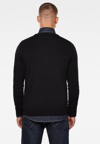 Schwarzer, gestrickter Pullover mit langen Ärmeln und rundem Ausschnitt, über einem Jeanshemd getragen, von hinten gezeigt.