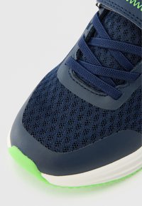 Ναυτικό αθλητικό παπούτσι με δίχτυ, με πράσινες λεπτομέρειες, που διαθέτει λεία σόλα από καουτσούκ και υφασμένη επικάλυψη κορδονιών για επιπλέον υποστήριξη.